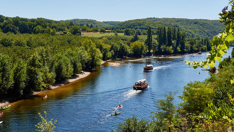 A scenic view of the Dordogne River with boats and kayaks, surrounded by lush greenery.