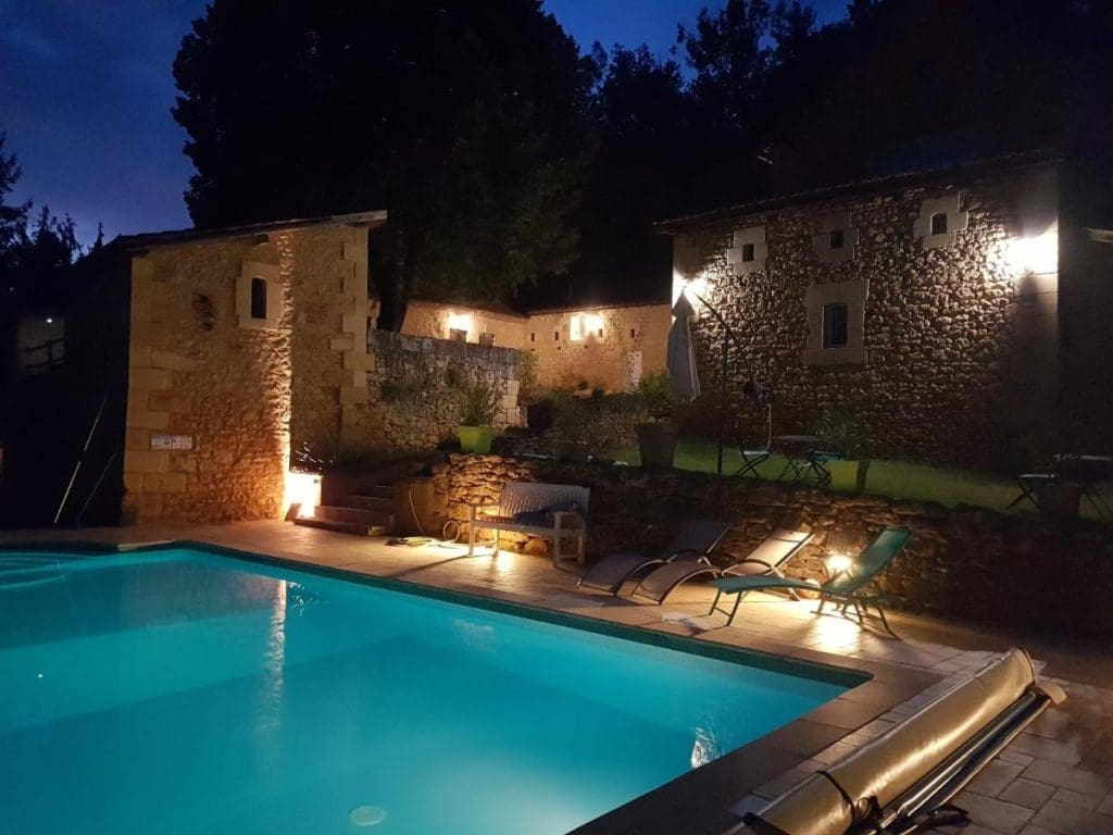 Le Clos de la Canéda's illuminated pool at night, surrounded by peaceful gardens.