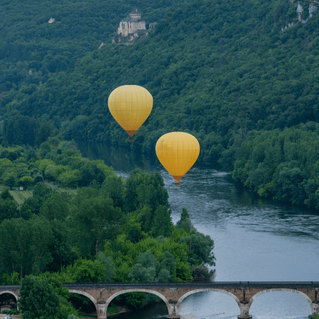 Two yellow hot air ballons flying over the Dordogne river with Chateau castlenaud in the backround