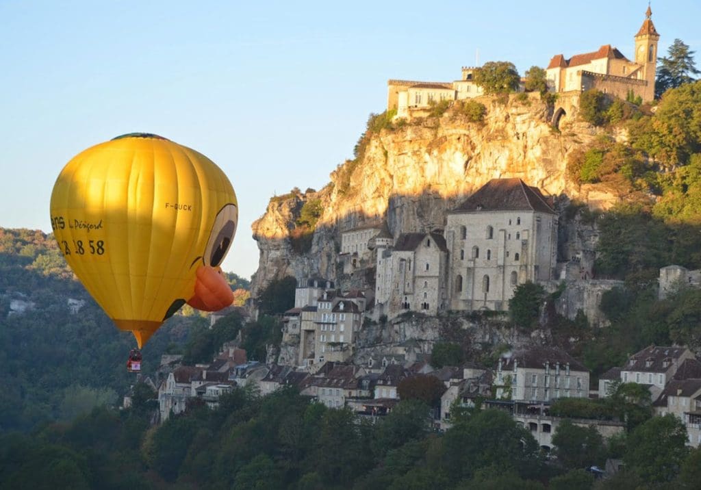 A hot air balloon shaped like a duck hovers above a medieval village