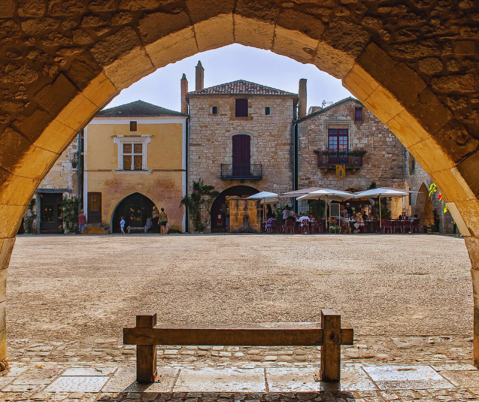 View of Monpazier’s market square, Place des Cornières, framed by a stone archway
